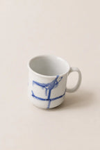 A white ceramic mug with a blue abstract painted design, set against a solid beige background.