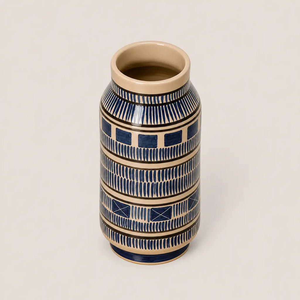 A small ceramic vase with a cream-colored interior and exterior base, decorated with navy blue geometric patterns and horizontal beige bands, set against a solid light beige background.