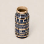 A small ceramic vase with a cream-colored interior and exterior base, decorated with navy blue geometric patterns and horizontal beige bands, set against a solid light beige background.