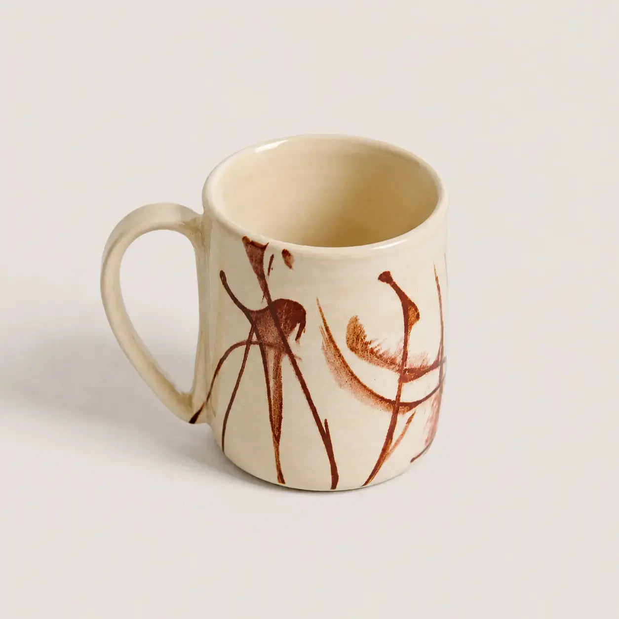 An off-white porcelain mug featuring a hand-painted abstract design in reddish-brown on the exterior, set against a plain light gray background.