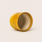 A small handmade ceramic espresso cup with a wide open top, featuring a textured mustard yellow glazed exterior and a matte beige interior, set against a plain off-white background.