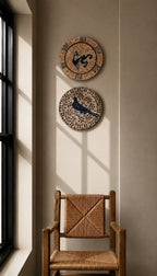 Two decorative circular wall clocks with bird motifs hang on a beige wall above a wooden armchair in a sunlit room.