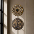 Two circular decorative wall plates with intricate patterns hang on a beige wall above a wooden chair with a woven seat, next to a window with soft sunlight.