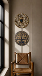 Two circular decorative wall plates with intricate patterns hang on a beige wall above a wooden chair with a woven seat, next to a window with soft sunlight.