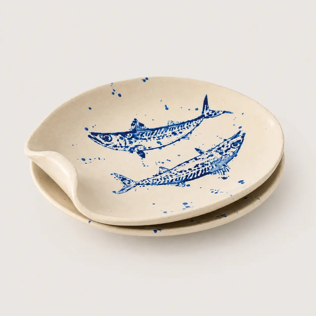 Set of two ceramic plates in a warm cream color, decorated with blue hand-painted fish and blue paint splatters, on a light gray background.