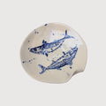 Cream-colored ceramic serving plate with blue hand-painted fish artwork, organic curved edges, and speckled detailing.