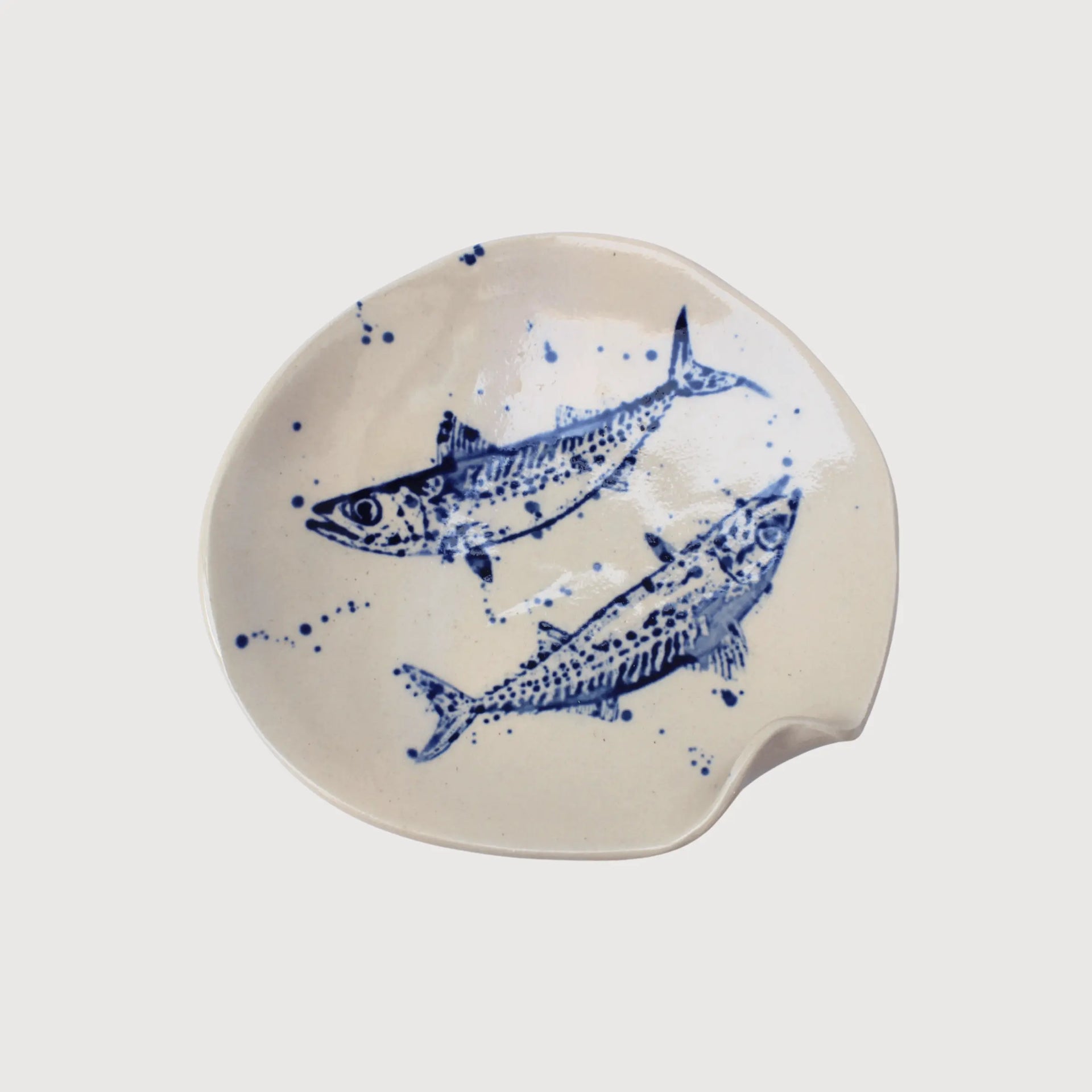 Cream-colored ceramic serving plate with blue hand-painted fish artwork, organic curved edges, and speckled detailing.