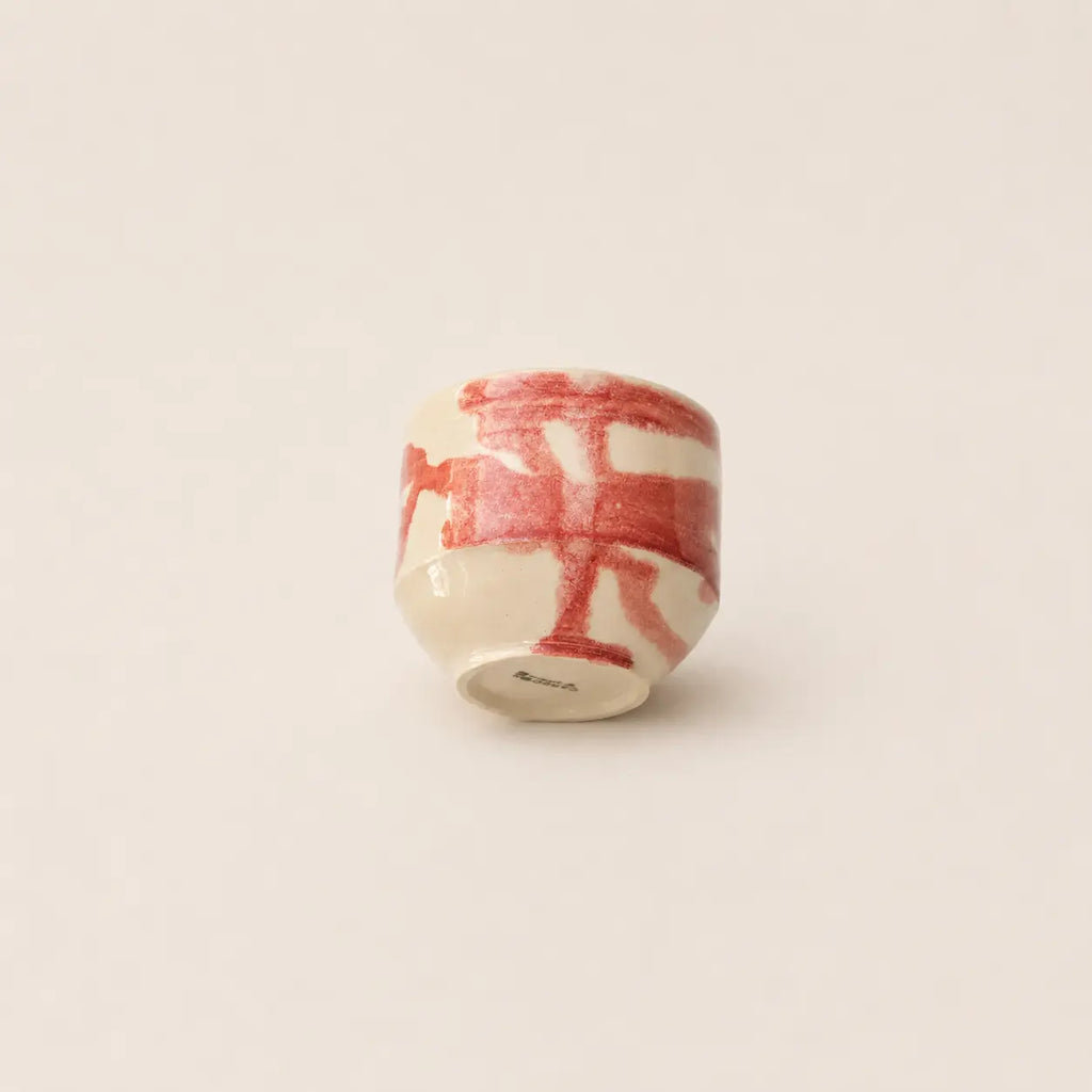 A small ceramic matcha cup with a glossy white glaze and bold red painted brushstrokes, shown from a top-down view on a plain off-white background.