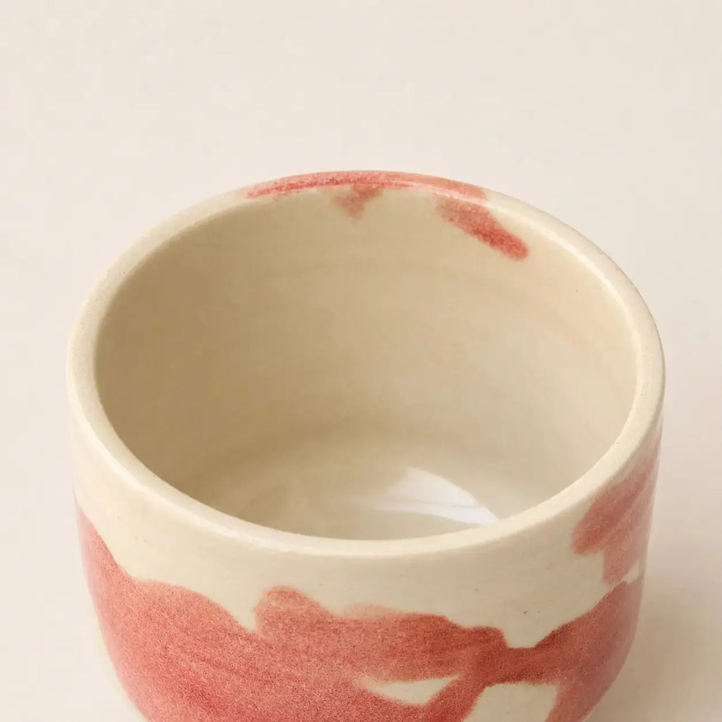 A handmade ceramic chawan matcha cup with a warm cream interior and a textured, hand-painted reddish-pink exterior, shown from a top-down angle on a light beige background.
