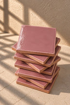 A stack of square dusty pink ceramic tiles on a textured beige surface.