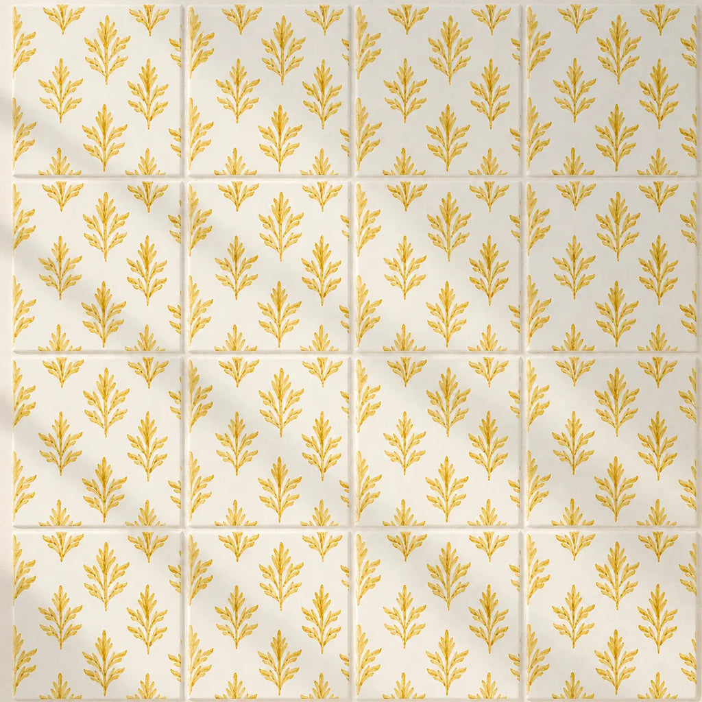 A repeating pattern of square tiles with a warm cream background and a metallic gold botanical leaf motif, arranged in a grid with thin grout lines.