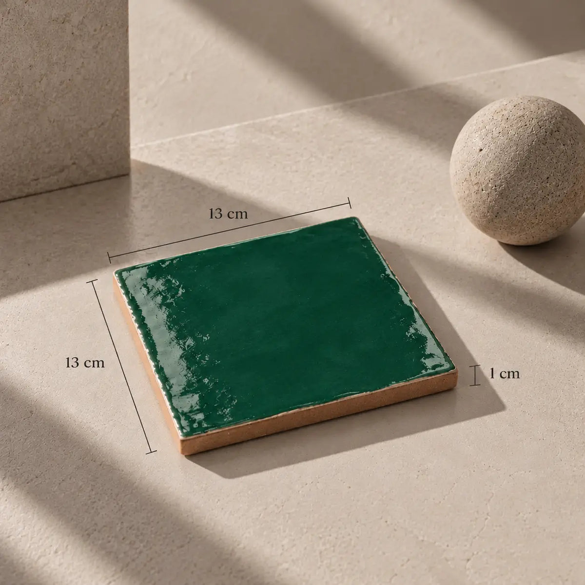 Glossy emerald green handmade ceramic tile, 13 x 13 cm and 1 cm thick, with hand-painted glaze and natural terracotta edges. Crafted in Spain.