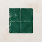 Four emerald green square tiles on a textured beige background