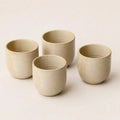Four small handmade ceramic espresso cup in a light beige stoneware finish, arranged on a plain off-white background.
