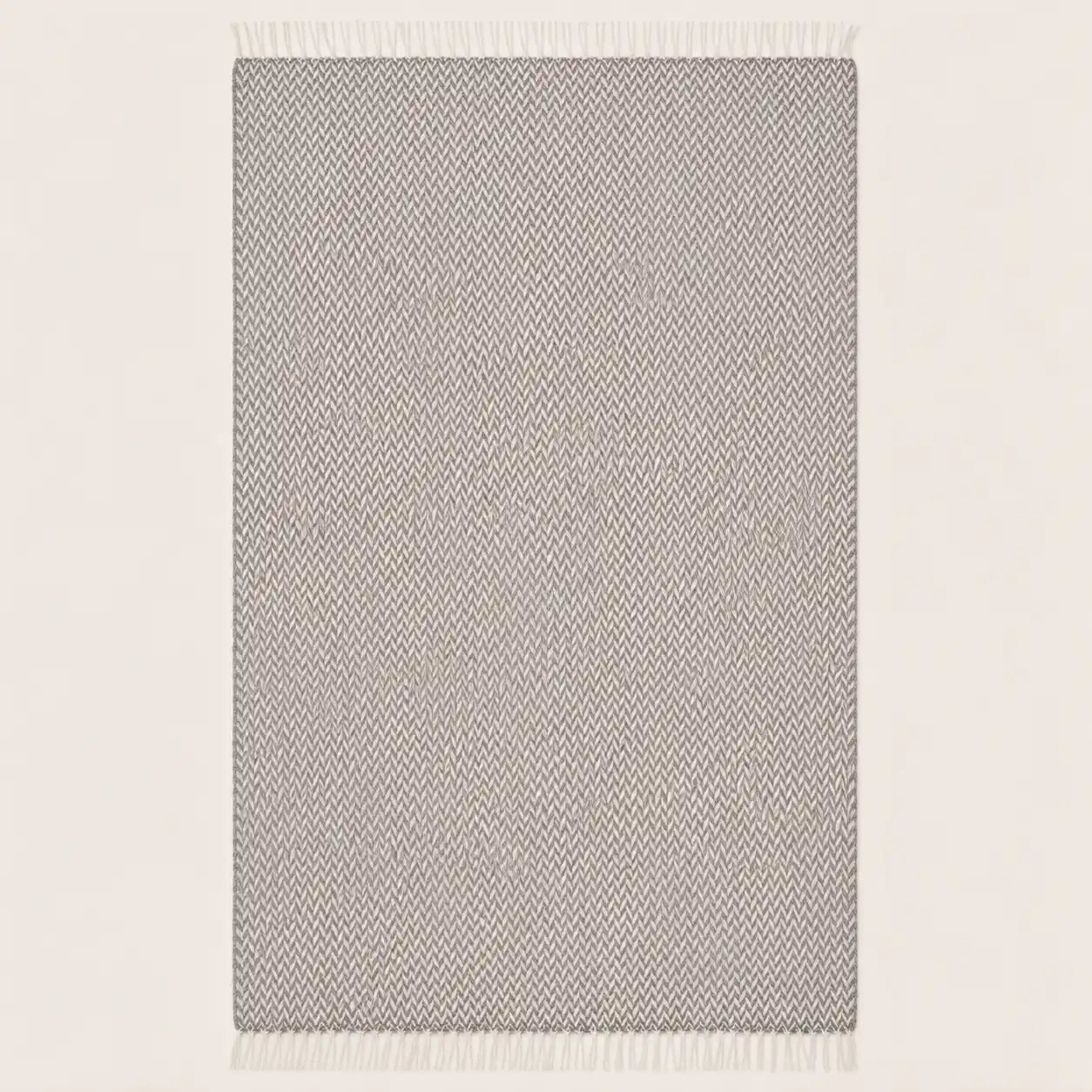 A rectangular throw blanket with a light gray and white textured herringbone pattern and white fringe on the top and bottom edges, shown against a plain off-white background.