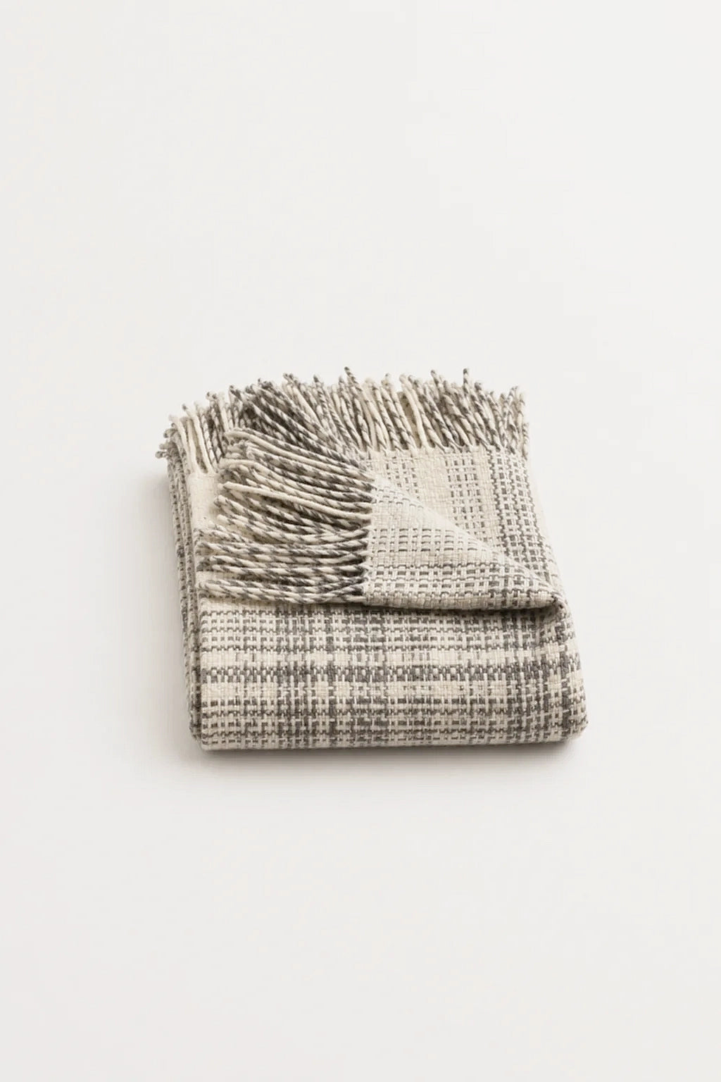 A folded woven throw blanket with fringed edges, shown on a plain white background. The blanket has a textured plaid pattern in off-white and gray.