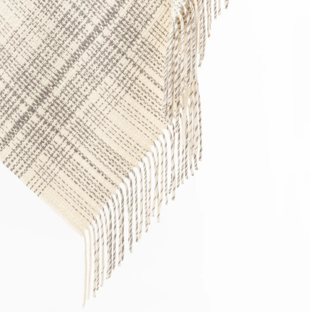 A cream and gray plaid fringed throw blanket draped over a light wood rod against a white background.