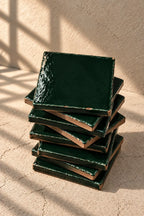 A stack of glossy forest dark green square coasters on a textured beige surface against a matching beige wall.