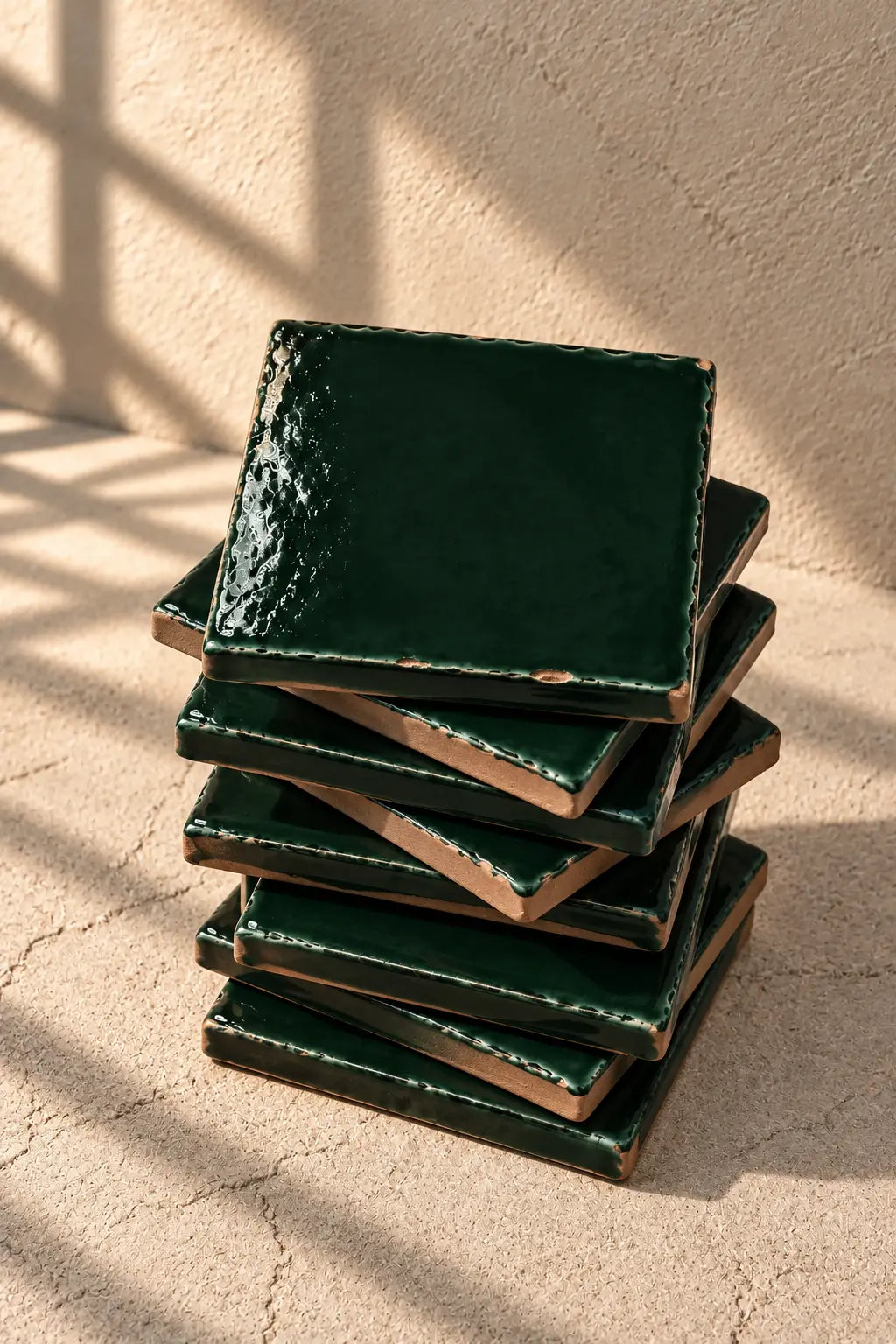 A stack of glossy forest dark green square coasters on a textured beige surface against a matching beige wall.
