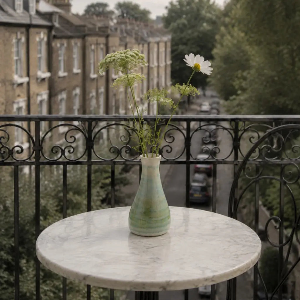 Vase with flowers on a marble table on a balcony with a view of buildings and trees.