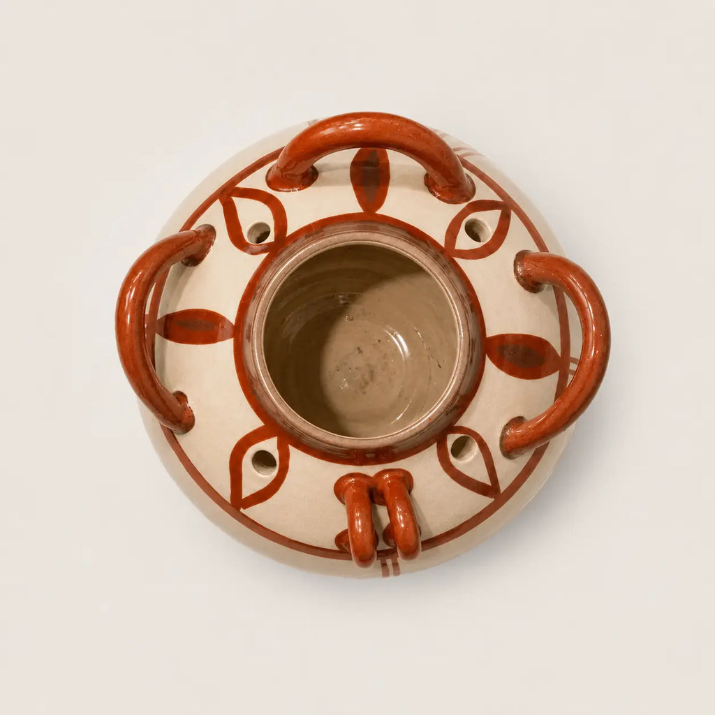 A top-down view of a round ceramic planter pot with a beige glaze and terracotta-colored handles and leaf-like patterns, set against a plain light background.