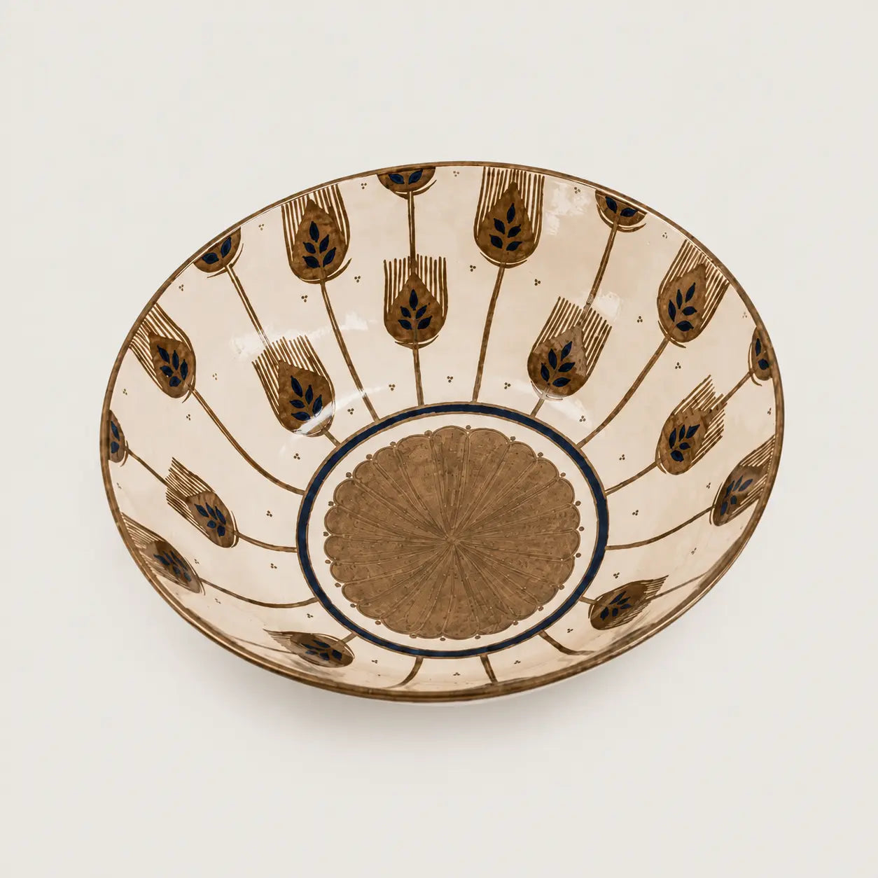 A round ceramic bowl with a cream-colored interior decorated with brown and black tulip-like motifs and a brown medallion in the center, shown on a light gray background.