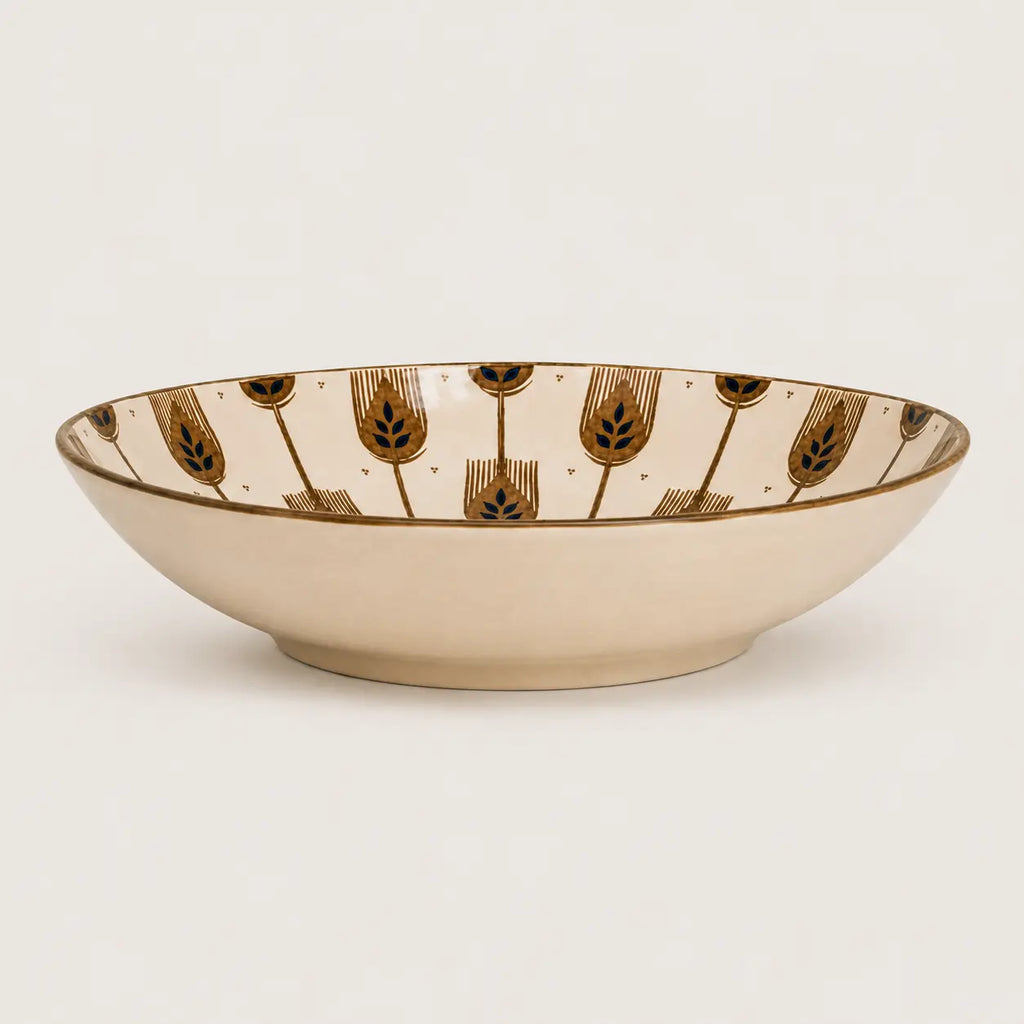 A shallow cream-colored ceramic bowl featuring a repeating pattern of stylized gold and dark blue-green botanical motifs on the interior rim, set against a plain light background.