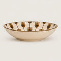 A shallow cream-colored ceramic bowl featuring a repeating pattern of stylized gold and dark blue-green botanical motifs on the interior rim, set against a plain light background.