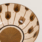 Close-up of a ceramic bowl showing its interior pattern, featuring a beige background decorated with brown and gold leaf-like motifs and a scalloped gold center.