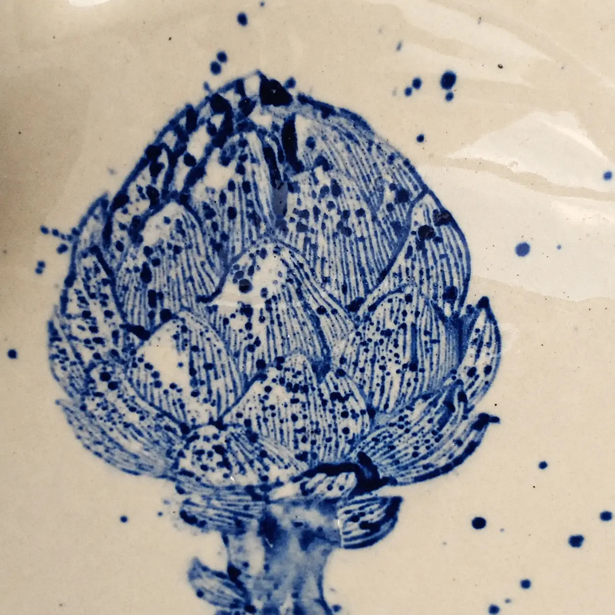 Close-up detail of intricate blue botanical artwork and speckled glaze on a handmade ceramic plate.