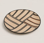 An oval ceramic plate with a geometric pattern of beige and cream stripes outlined in black, accented with thin brown lines, on a light beige background.