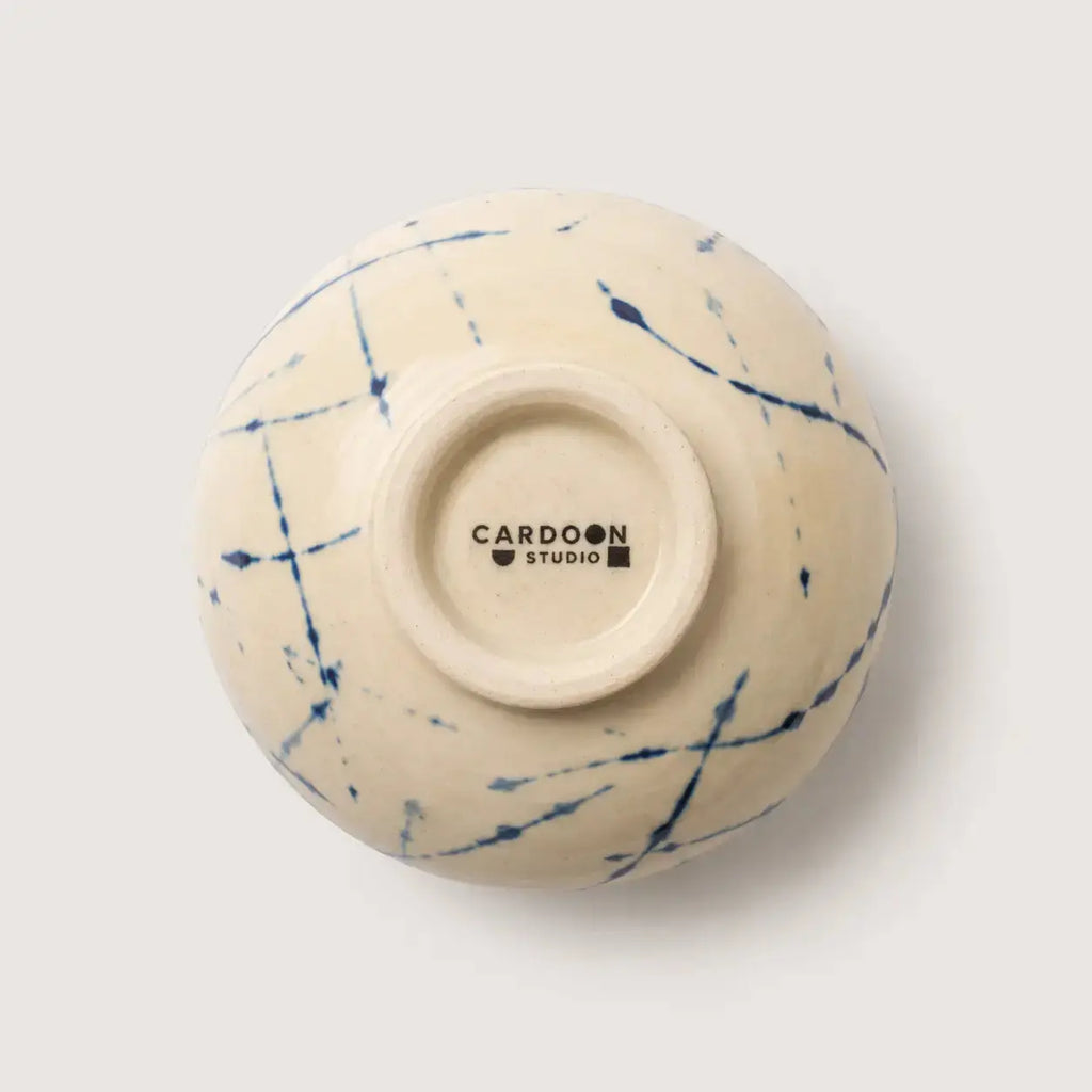 An off-white ceramic snack bowl viewed from underneath, featuring a blue ink-blot style pattern on the exterior and the brand name 'CARDON STUDIO' printed in black on the center base.