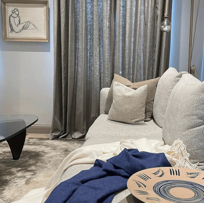 Cozy contemporary living room with textured neutral furnishings, layered textiles, and handcrafted ceramic decor in soft ambient light.