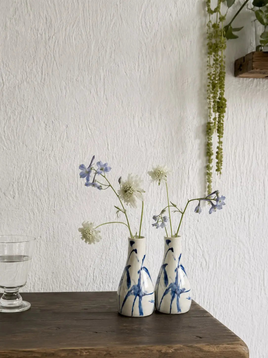 Two small ceramic vases with blue floral patterns on a wooden surface against a white wall.