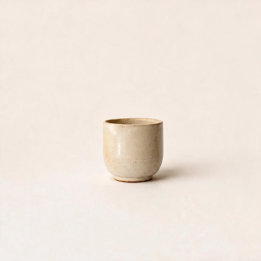 White ceramic cup with gold rim on a matching saucer against a white background
