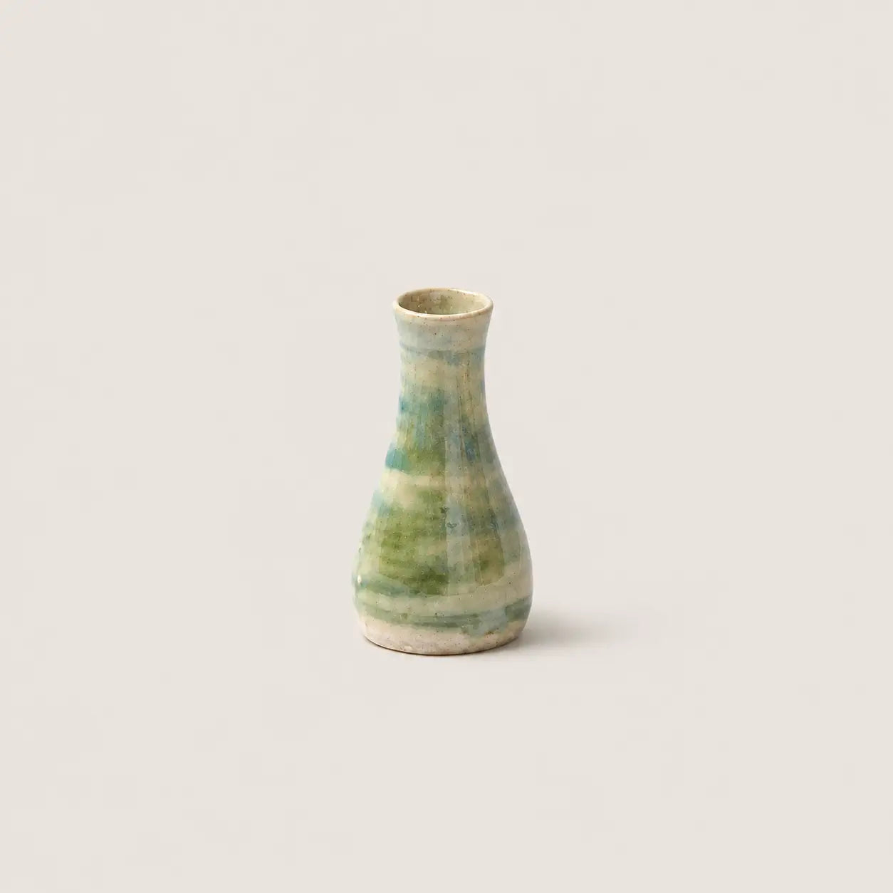 A small handmade ceramic bud vase with a green and beige marbled glaze, centered against a solid light beige background.