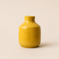 A small glossy ceramic vase in a warm mustard yellow color, centered against a solid, light beige background.