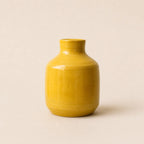 A small glossy ceramic vase in a warm mustard yellow color, centered against a solid, light beige background.