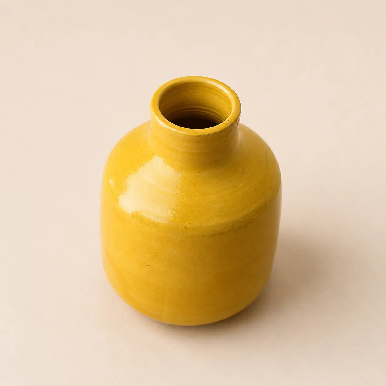 A small glossy ceramic vase with a rounded body and short neck, finished in a warm mustard yellow glaze, set against a plain light beige background.