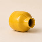 A small glossy ceramic vase in a warm mustard yellow color, centered against a solid, light beige background.