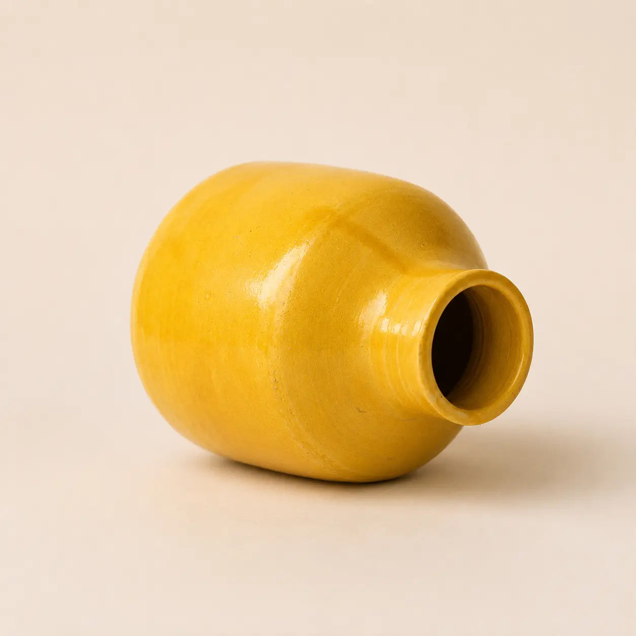 A small glossy ceramic vase in a warm mustard yellow color, centered against a solid, light beige background.