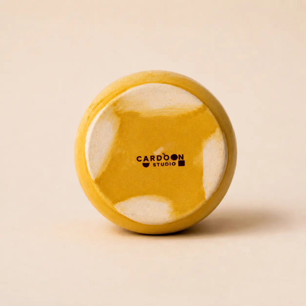 A small glossy ceramic vase in a warm mustard yellow color, centered against a solid, light beige background.