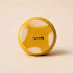 A small glossy ceramic vase in a warm mustard yellow color, centered against a solid, light beige background.