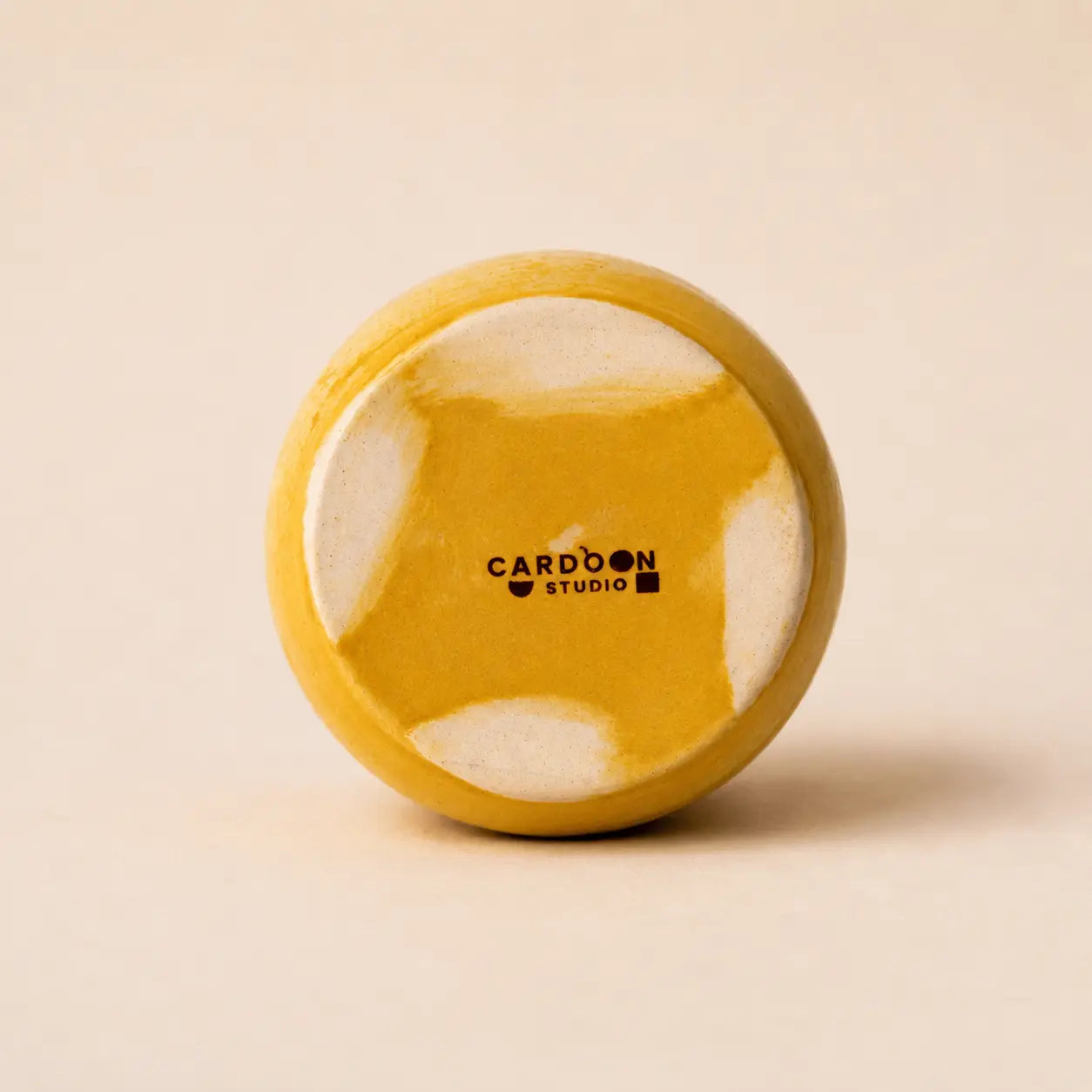 A small glossy ceramic vase in a warm mustard yellow color, centered against a solid, light beige background.