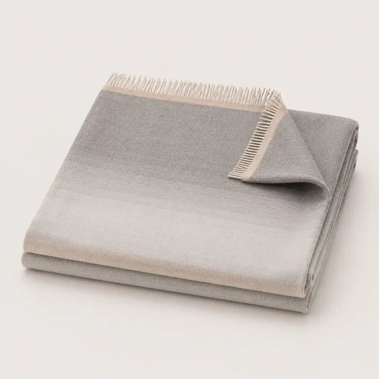 A folded light gray throw blanket with a subtle gradient and fringed edge, displayed on a clean off-white background.