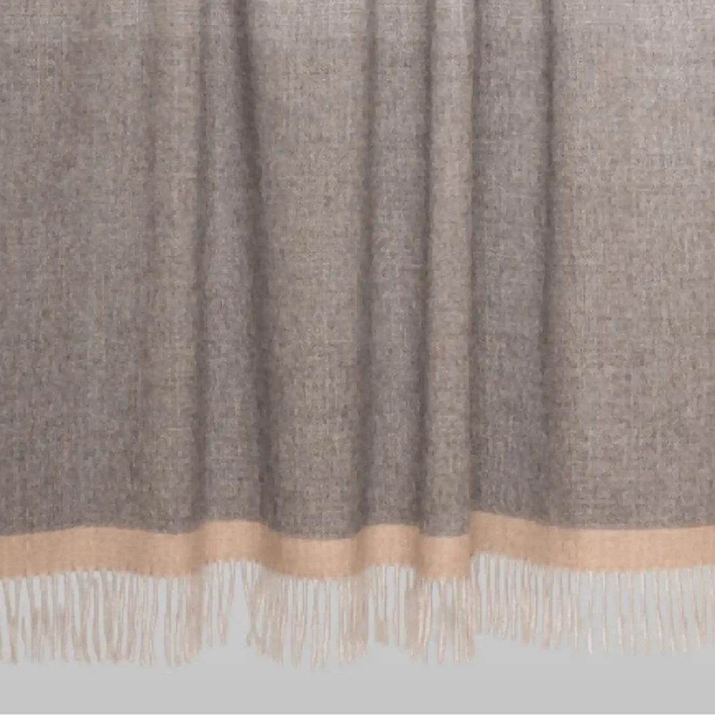 Textured throw blanket with a gradient pattern and fringed edge on a light gray background