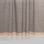 Textured throw blanket with a gradient pattern and fringed edge on a light gray background