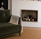 Green sofa with a throw blanket in alpaca next to a fireplace in a living room.
