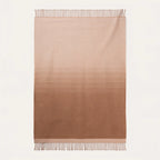 A rectangular woven throw blanket with a vertical ombré gradient transitioning from light beige at the top to a medium warm brown at the bottom, finished with fringed edges on a white background.