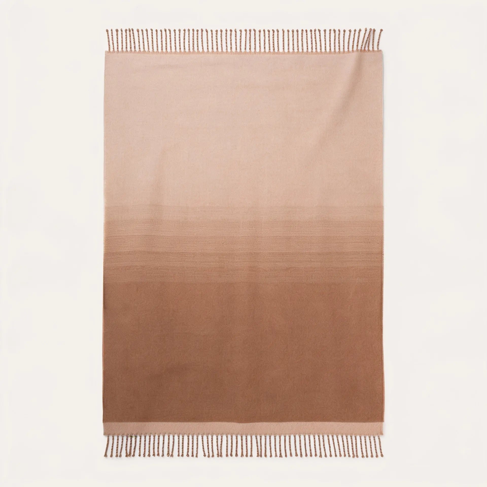 A rectangular woven throw blanket with a vertical ombré gradient transitioning from light beige at the top to a medium warm brown at the bottom, finished with fringed edges on a white background.